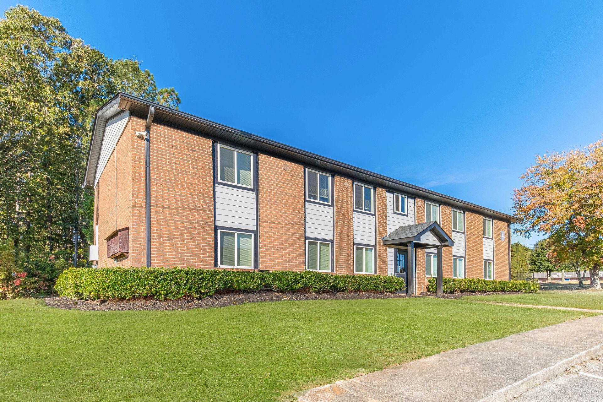 Two-story brick apartment building with green lawns under a clear blue sky