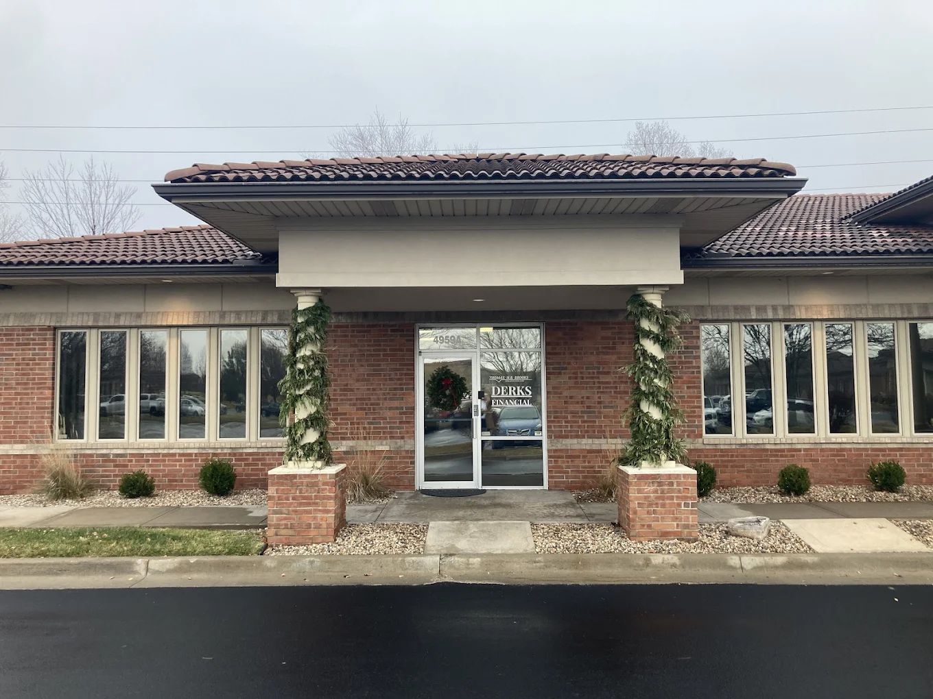 Brick building with a glass door entrance, columns wrapped with garland, topped with terracotta tile roof.