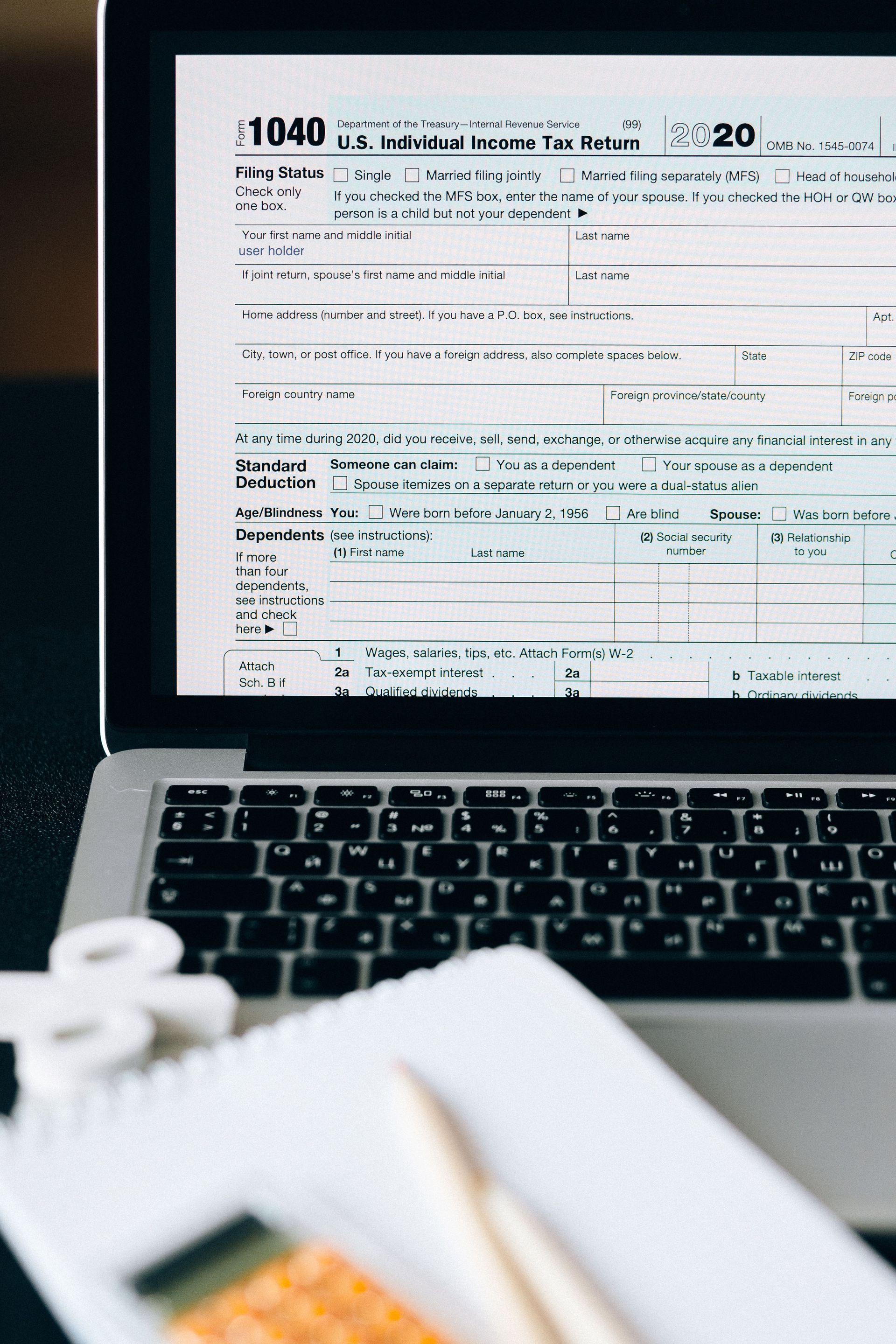 Laptop displaying a tax form beside a notepad and pencil on a desk