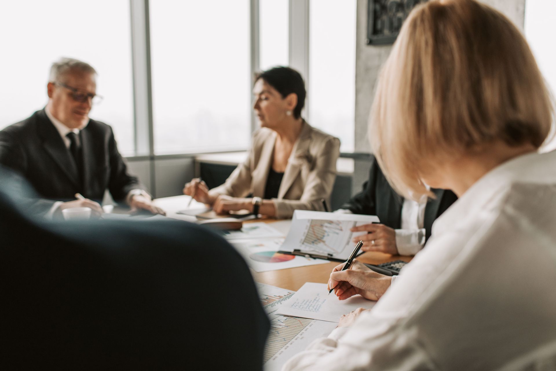 Business meeting around a table with documents, laptops, and people discussing in a bright office.