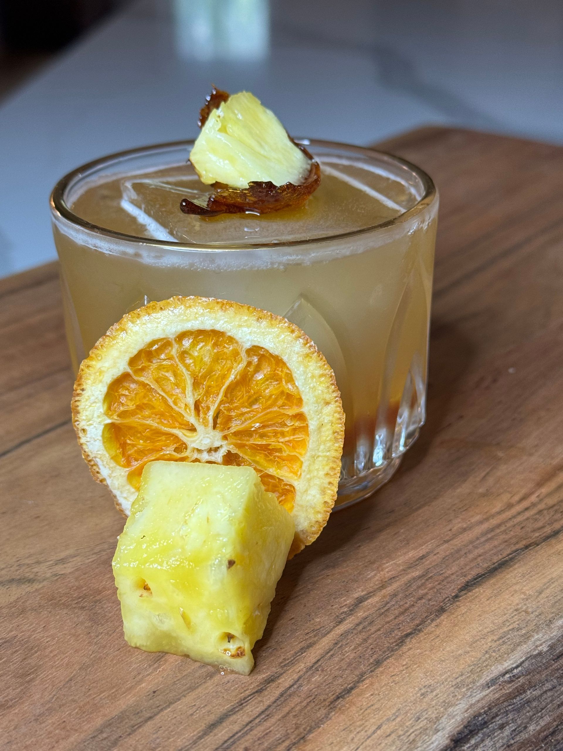 A close up of a drink with pineapple and orange slices on a wooden table.