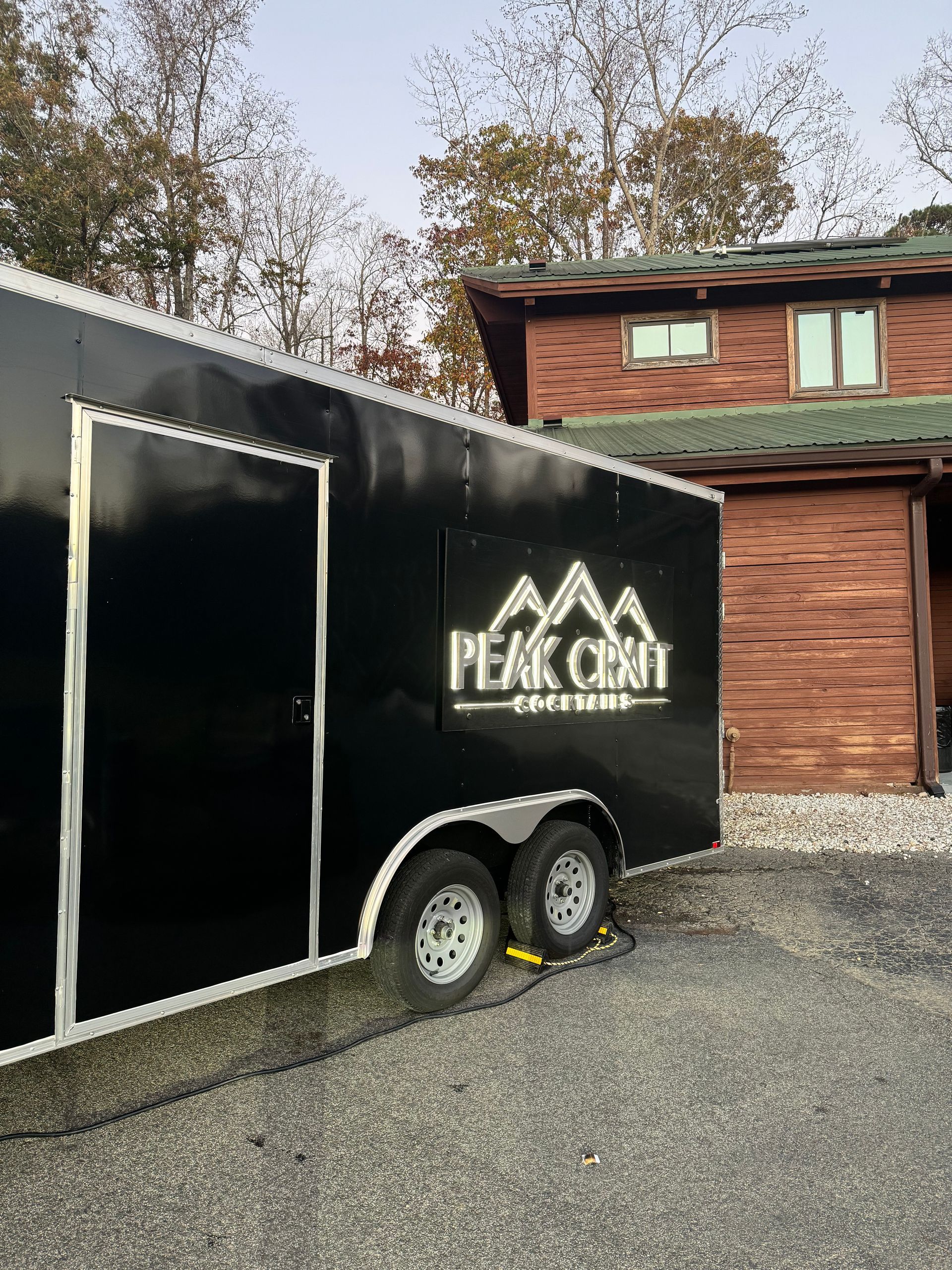 A black trailer is parked in front of a wooden house.