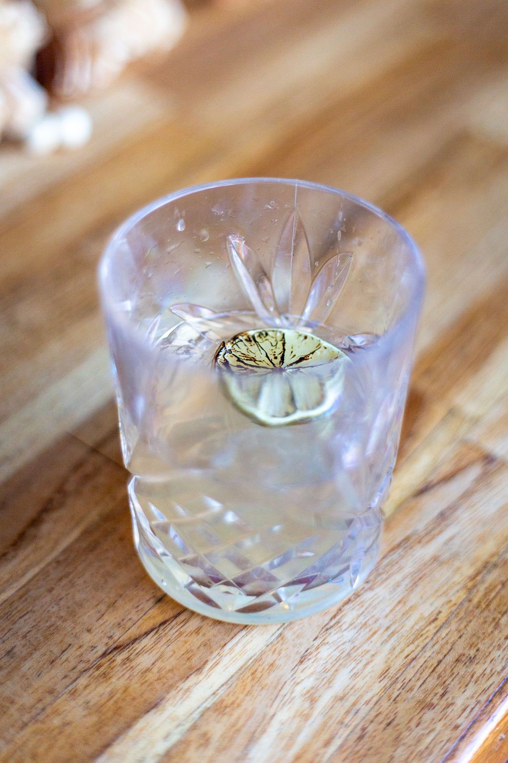 A glass of water with a slice of lime on a wooden table.