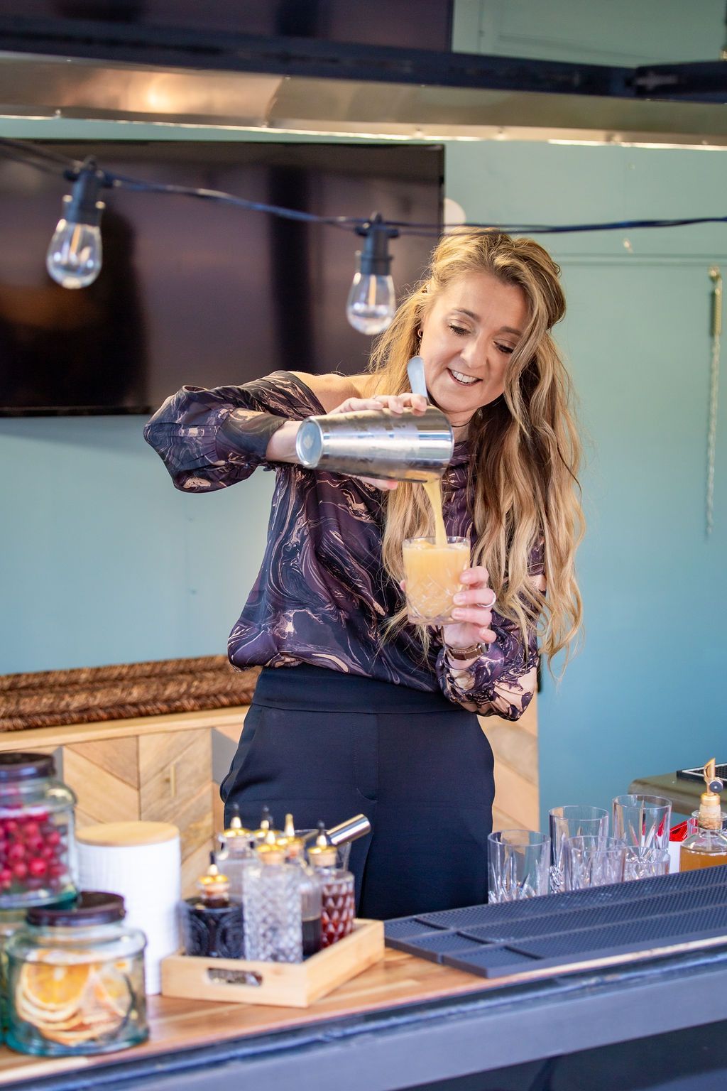 A woman is pouring a drink from a shaker into a glass.