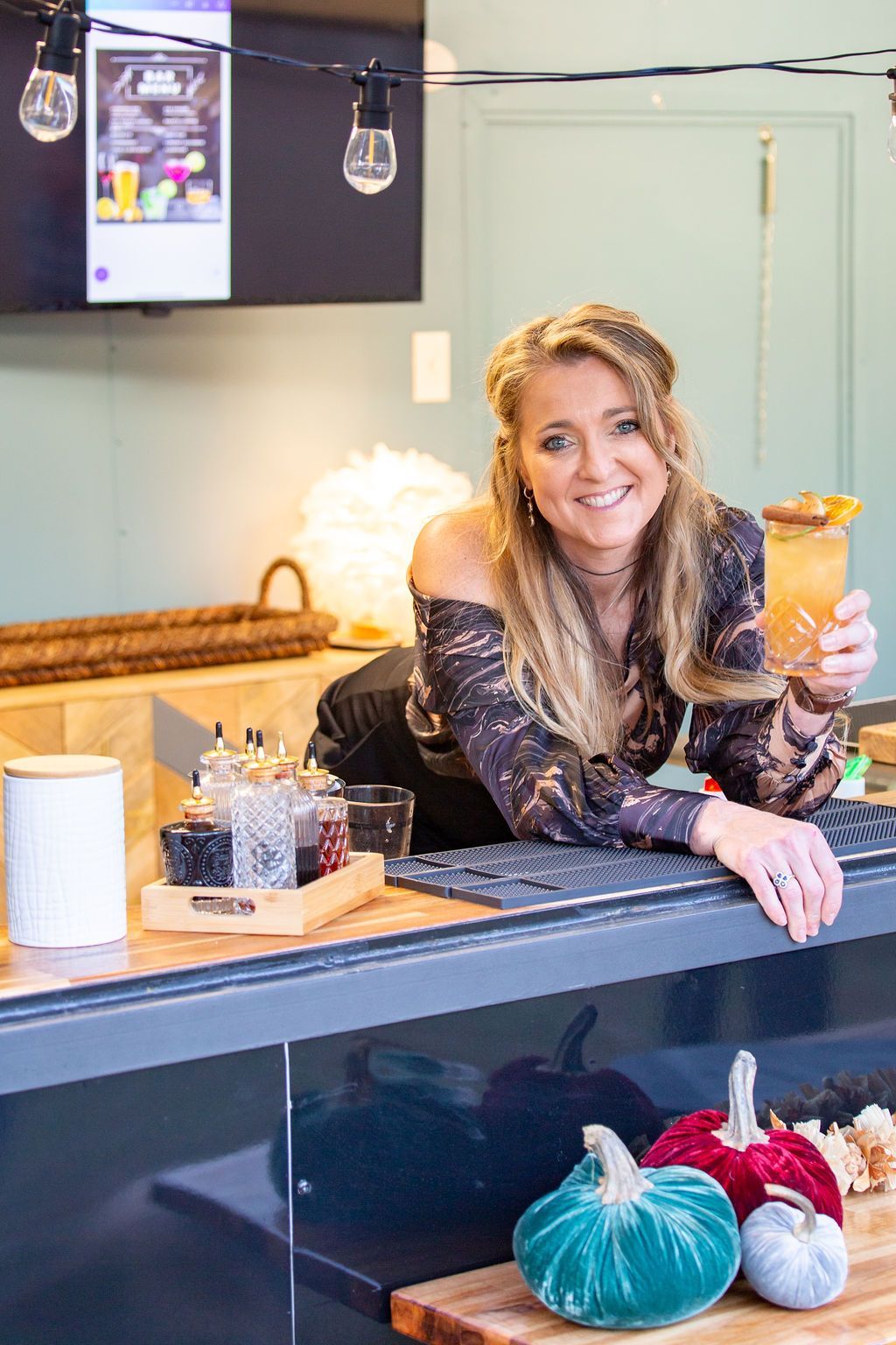 A woman is leaning on a counter holding a drink.