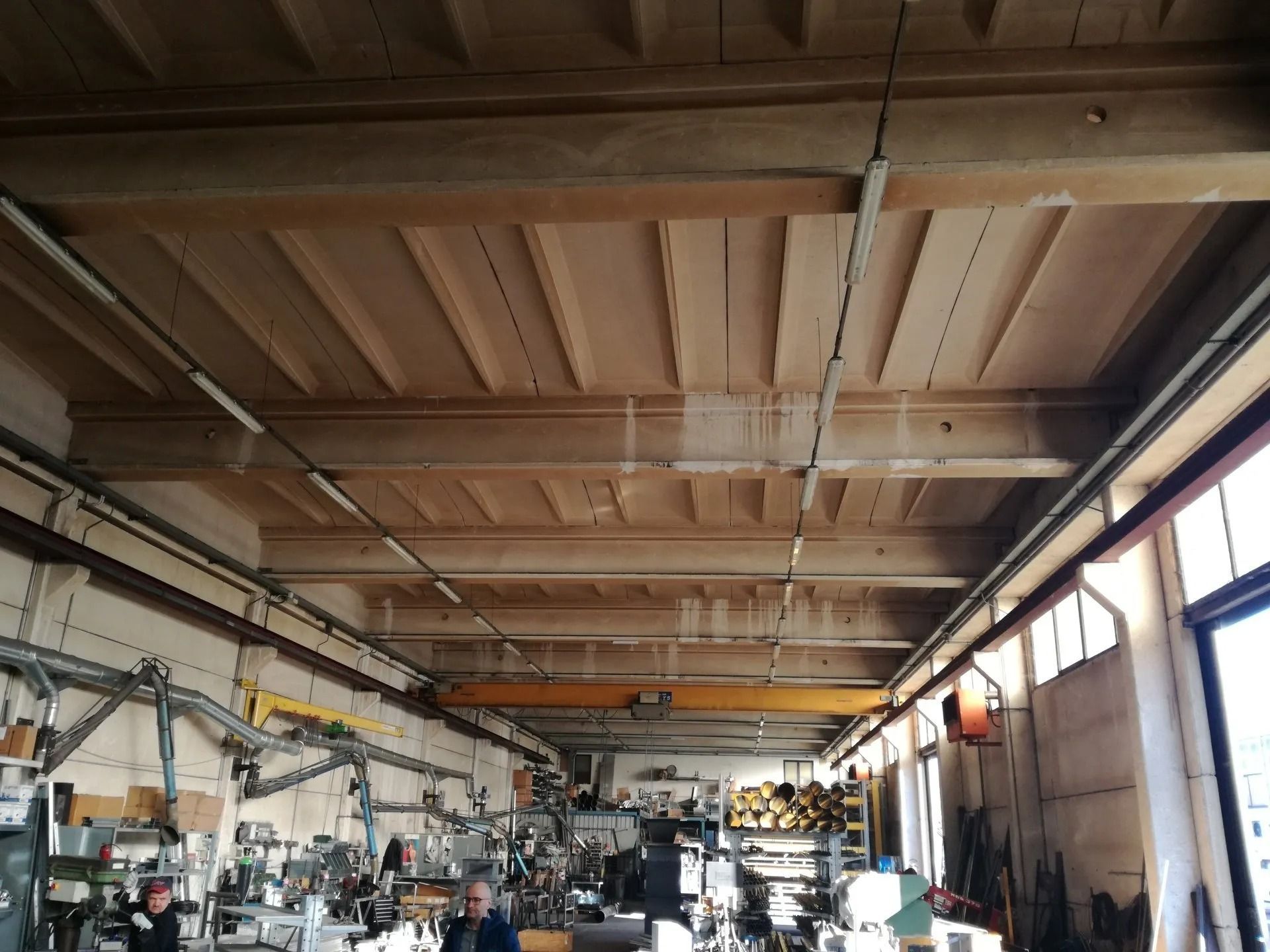 Interno di un'officina con un alto soffitto in legno, macchinari e grandi finestre lungo la parete destra.