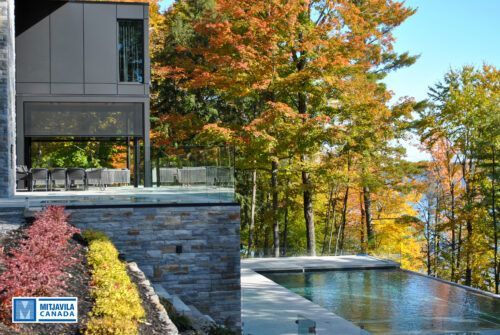 Maison moderne avec terrasse donnant sur une piscine et des arbres aux couleurs d'automne.