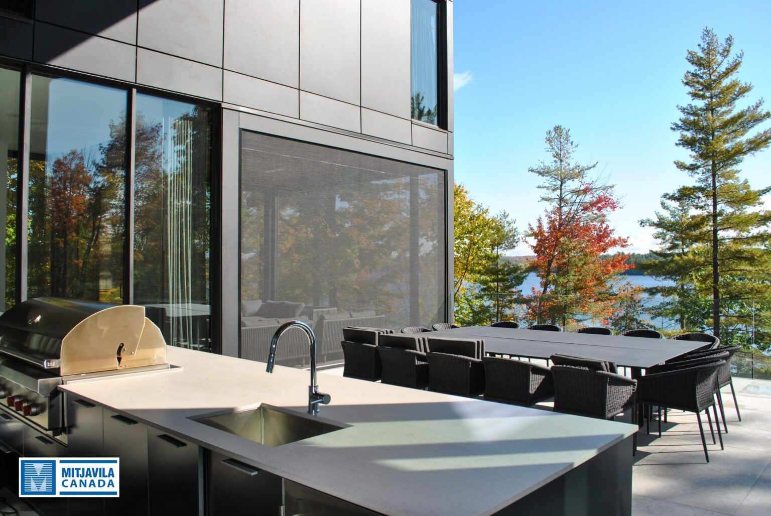 Cuisine extérieure avec barbecue, évier et table à manger donnant sur le lac et les arbres.