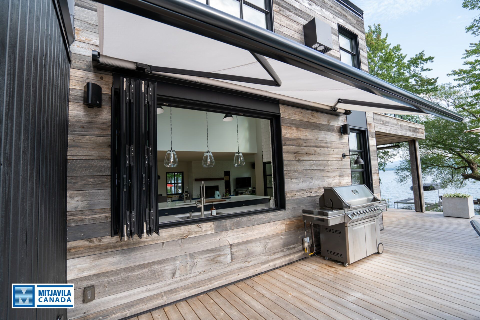 Extérieur d'une maison moderne avec porte accordéon ouverte, auvent extensible et barbecue sur une terrasse en bois.