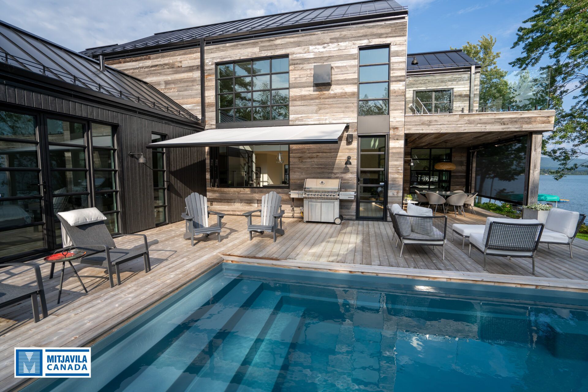 Maison moderne avec piscine, terrasse extérieure et vue sur le lac. Bardage gris et noir, fenêtres à cadre foncé.