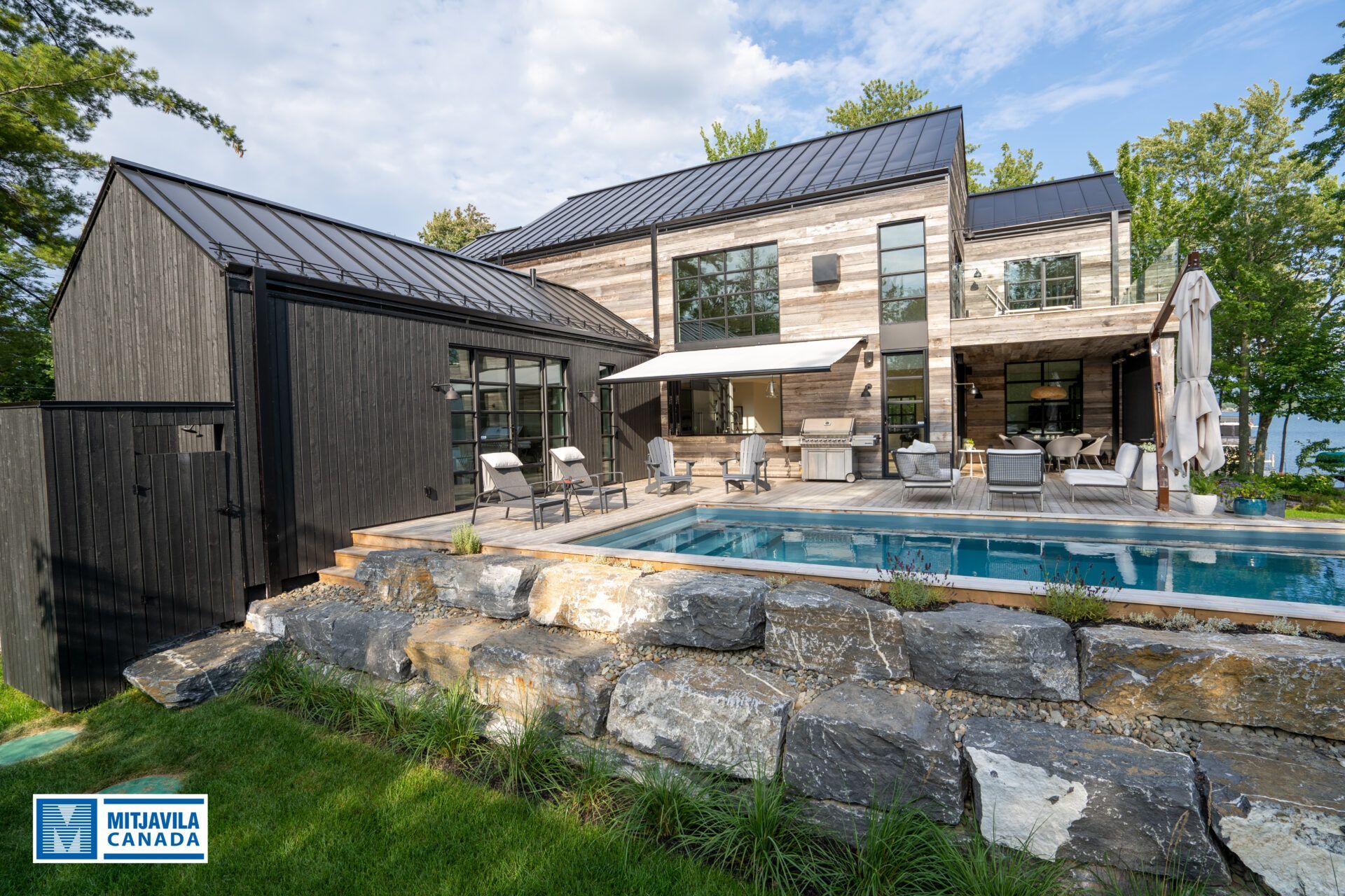 Maison moderne avec bardage noir, piscine, coin salon ext&eacute;rieur et vue sur l'eau.