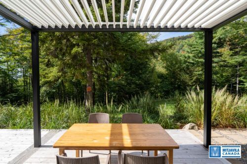 Espace repas ext&eacute;rieur avec table en bois, chaises et pergola donnant sur la verdure.