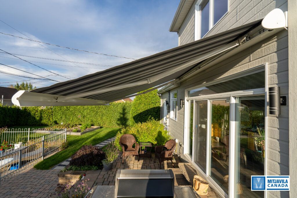 Store rétractable gris au-dessus d'une porte coulissante en verre, s'étendant au-dessus d'une terrasse avec vue sur le jardin.