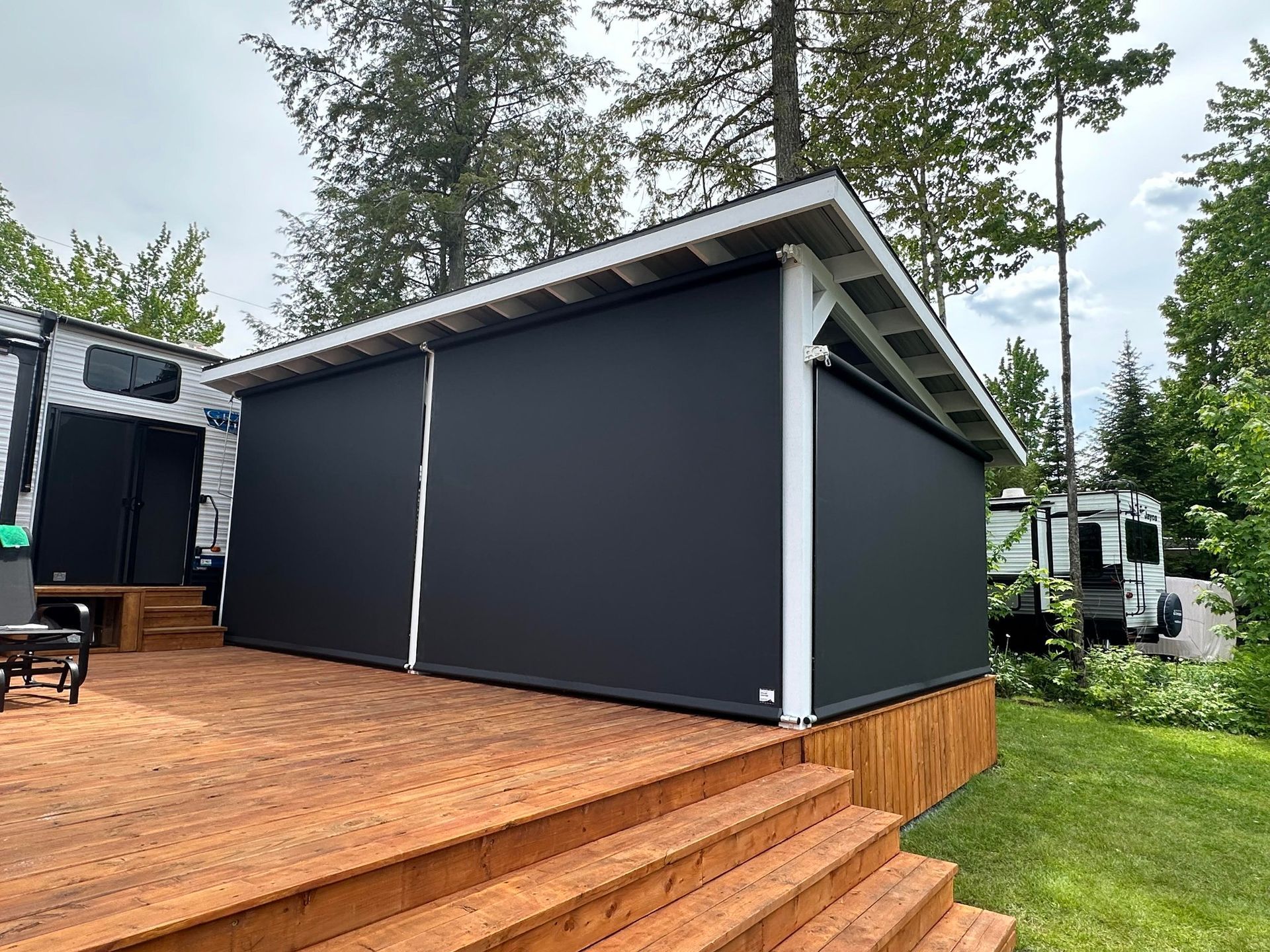 Terrasse en bois avec une structure couverte équipée de stores noirs rétractables ; environnement de camping.