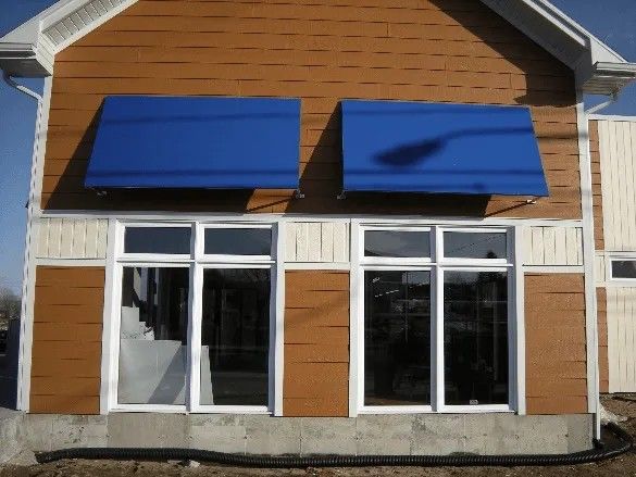 Façade du bâtiment avec bardage brun, deux auvents bleus au-dessus des fenêtres.