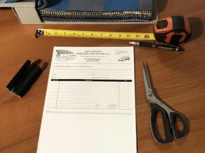 Outils et matériaux sur une surface en bois, notamment du tissu, un mètre ruban, une facture, un stylo, des ciseaux et des objets emballés.