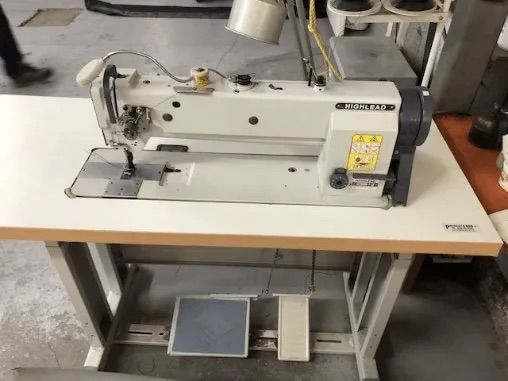 Machine à coudre sur une table blanche dans un environnement industriel, avec pédale.