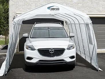 Un SUV blanc est garé sous un abri de voiture portable blanc et gris, sur une allée.