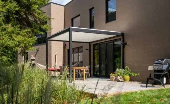 Patio moderne avec portes vitrées, pergola blanche, plantes en pot et barbecue à côté d'une maison.