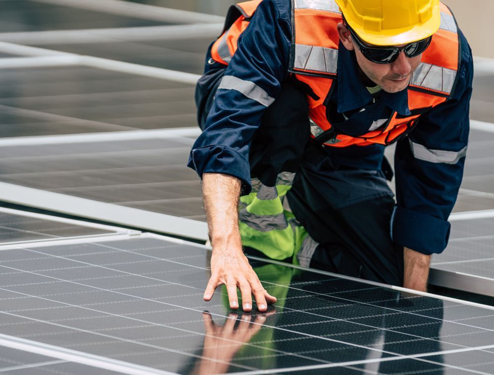 Worker in hard hat and safety vest inspecting solar panels on a rooftop