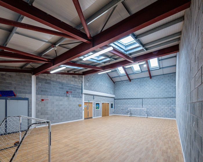 An indoor sports hall with wooden floors, grey block walls, exposed steel beams, and ceiling skylights.