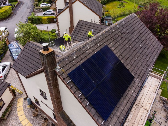 Workers in high-visibility yellow jackets installing solar panels on a tiled residential roof.