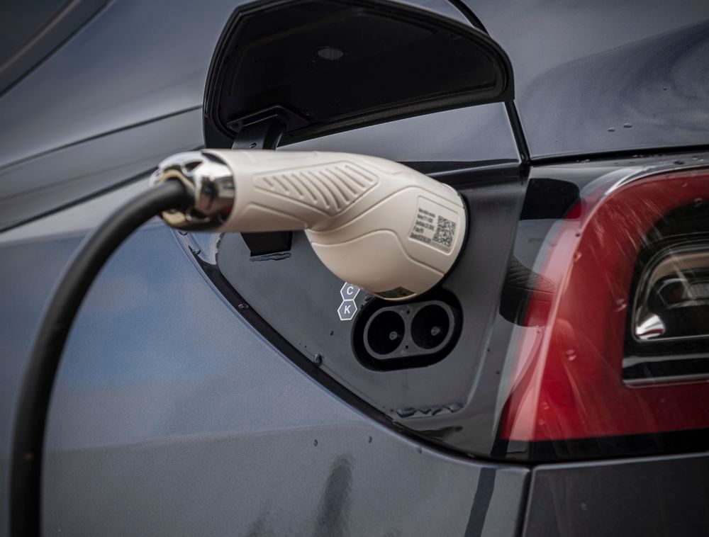 A white electric vehicle charging plug connected to a dark-colored car's charging port.