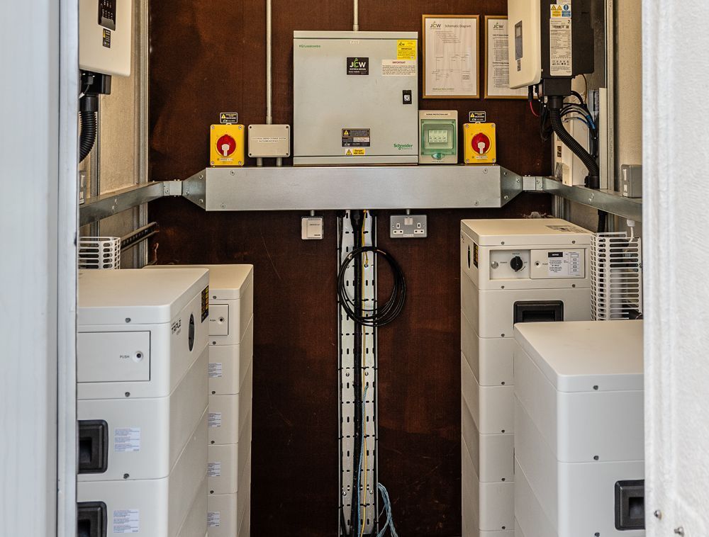 Utility room with wall-mounted electrical panels, switches, and white vertical battery storage units.