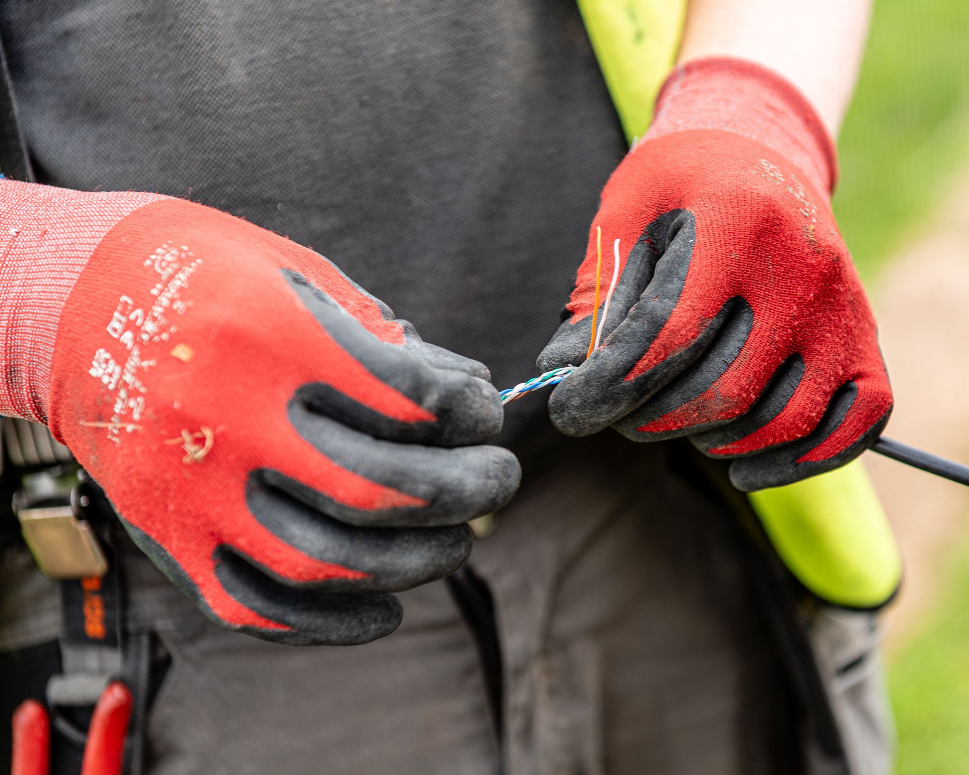 A person wearing red and black work gloves untwisting small, colored electrical wires.