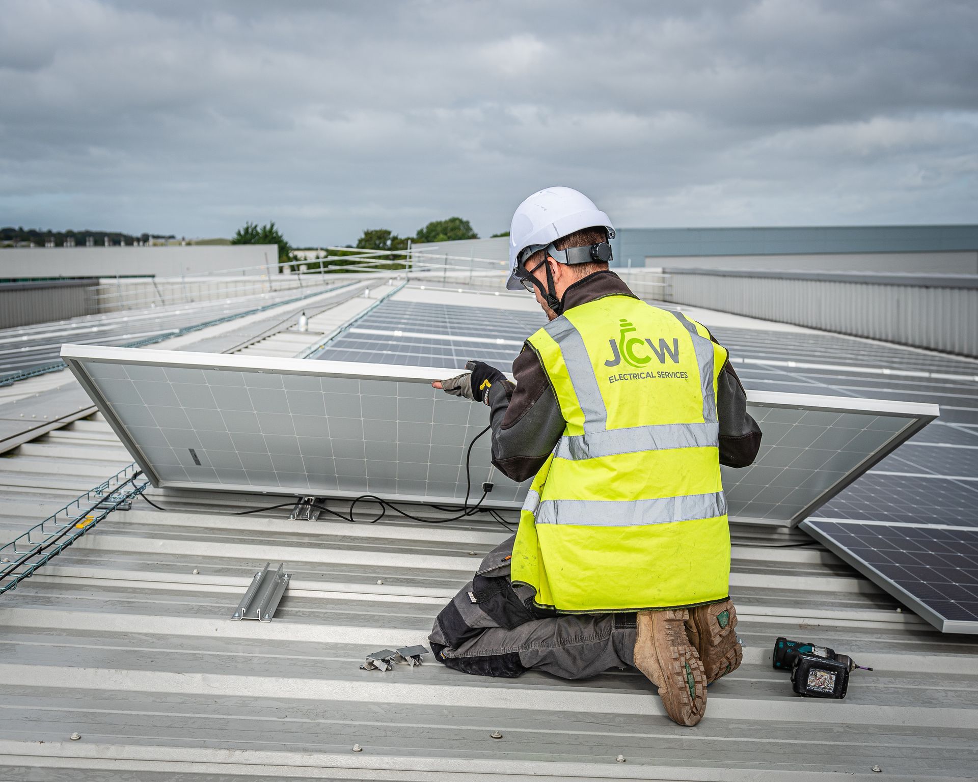A technician in a high-visibility vest kneels on a rooftop, wiring a solar panel into place.