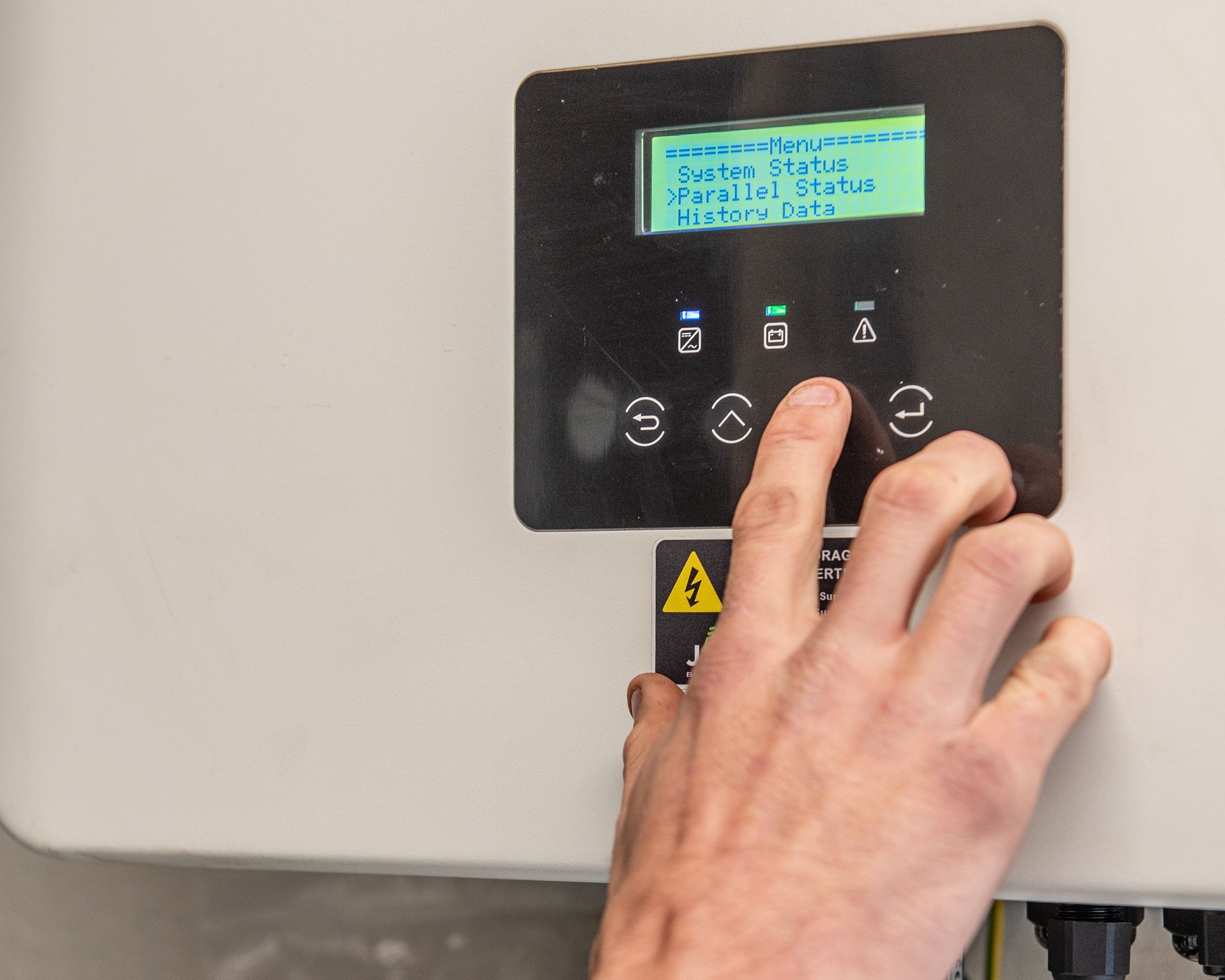 A hand adjusts the settings on a digital display panel for a solar inverter mounted on a wall.