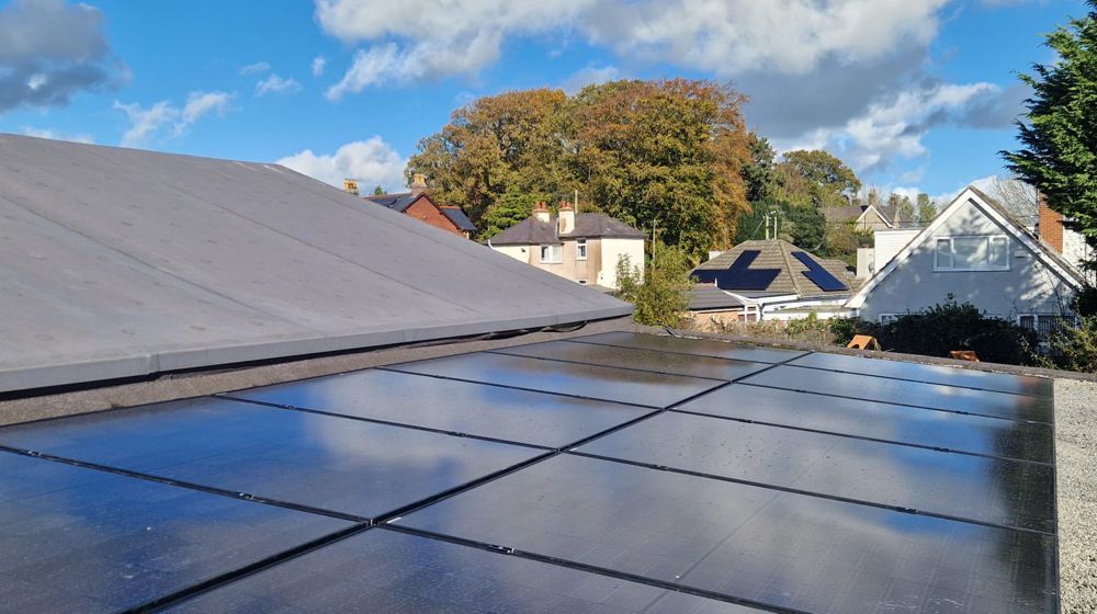Solar panels installed on a residential roof under a blue sky with clouds, next to neighboring homes.