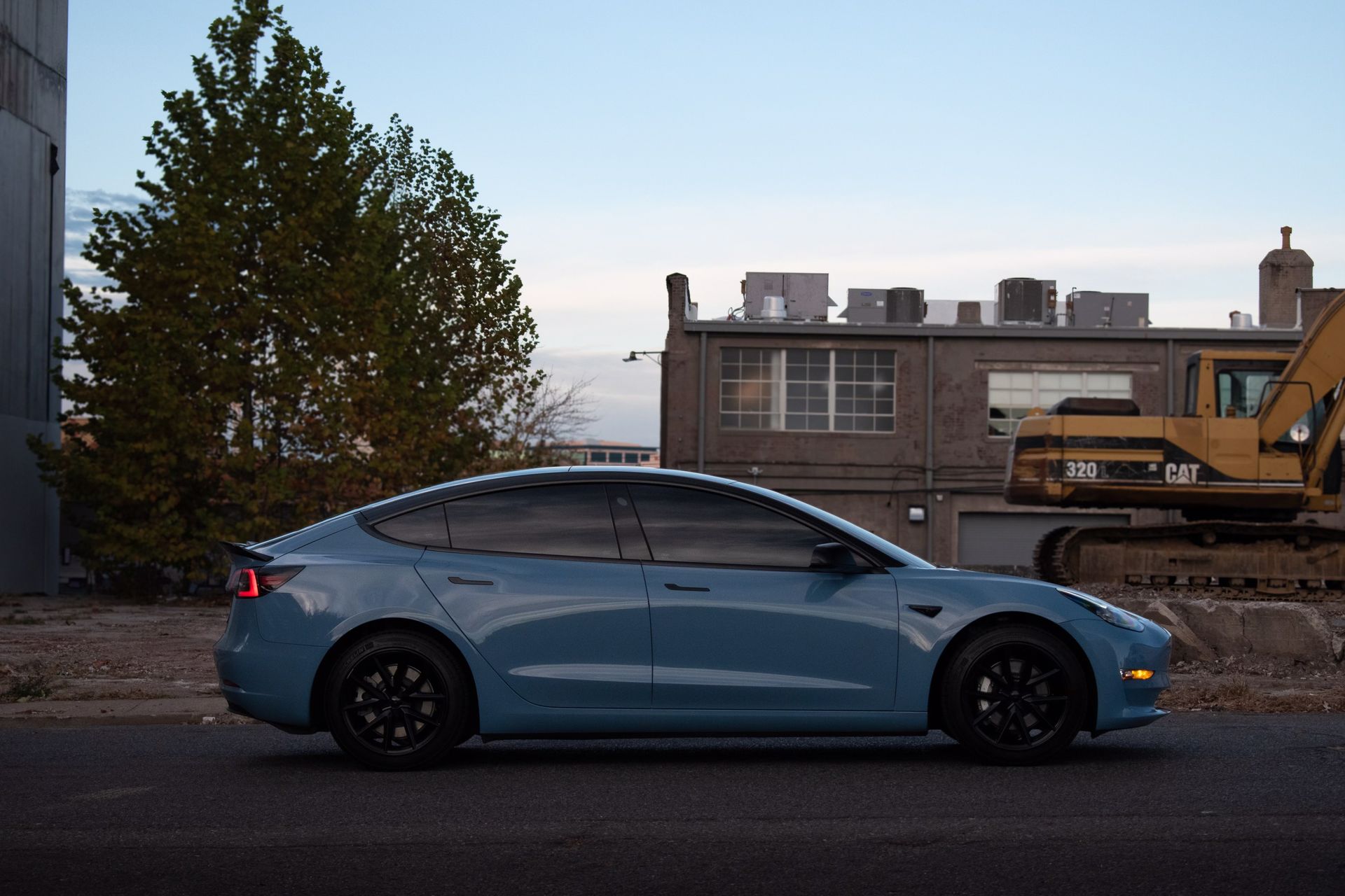 a blue tesla model 3 is parked on the side of the road in front of a building.