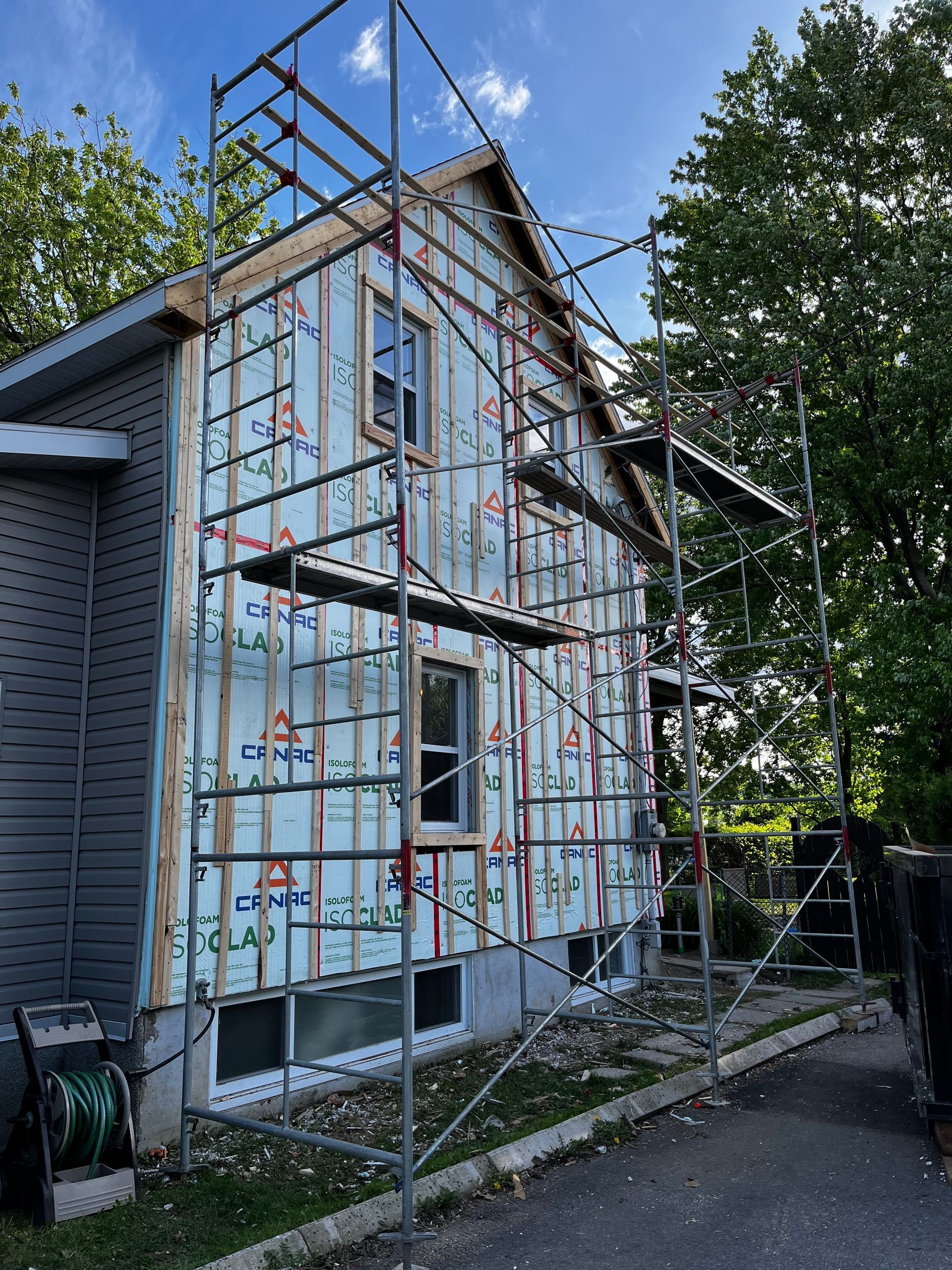 Façade d'une maison en construction avec échafaudages. Bardage gris, charpente en bois apparente et isolation bleue.