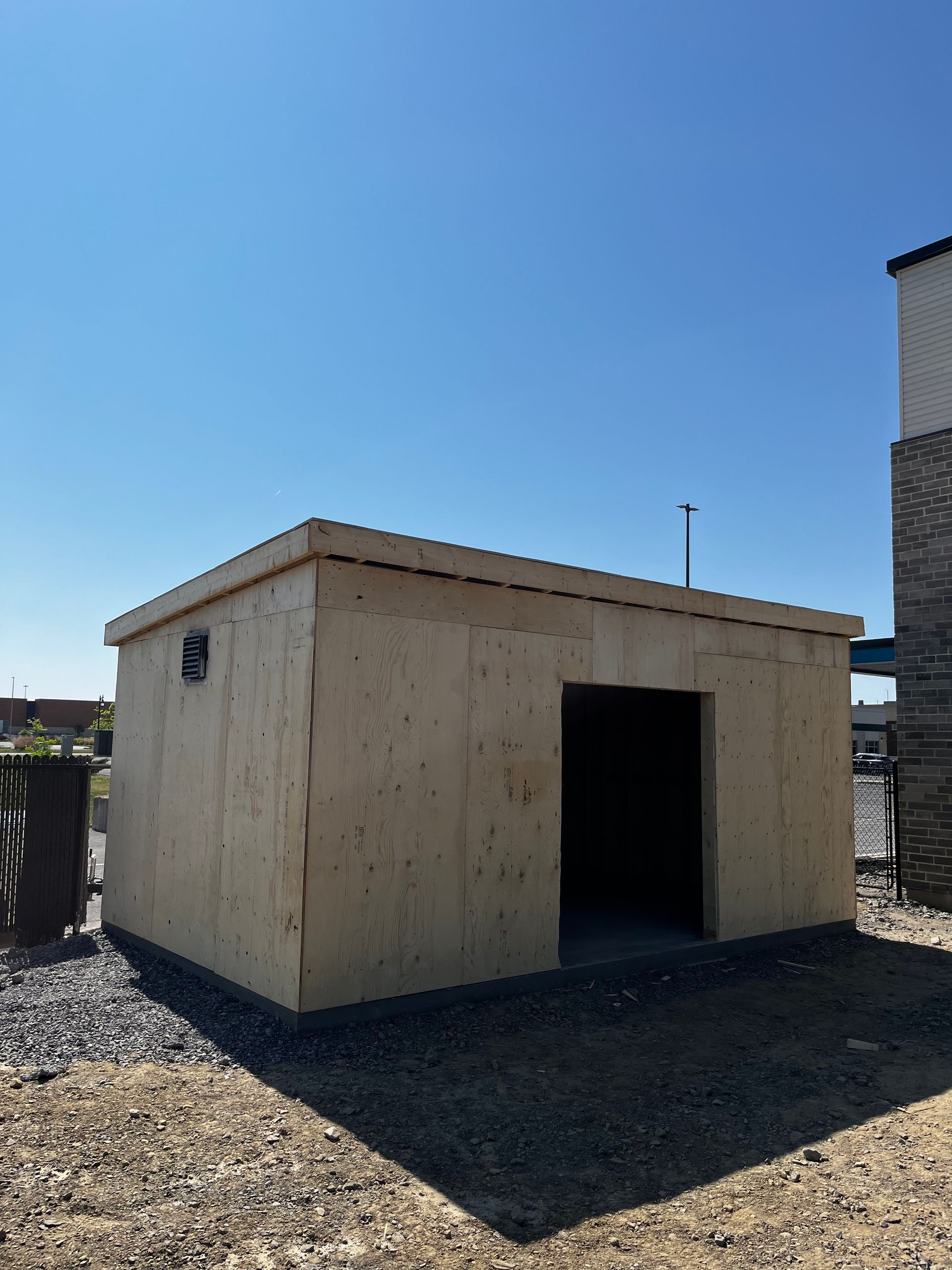 Abri de jardin en bois avec porte ouverte se détachant sur un ciel bleu, posé sur du gravier.