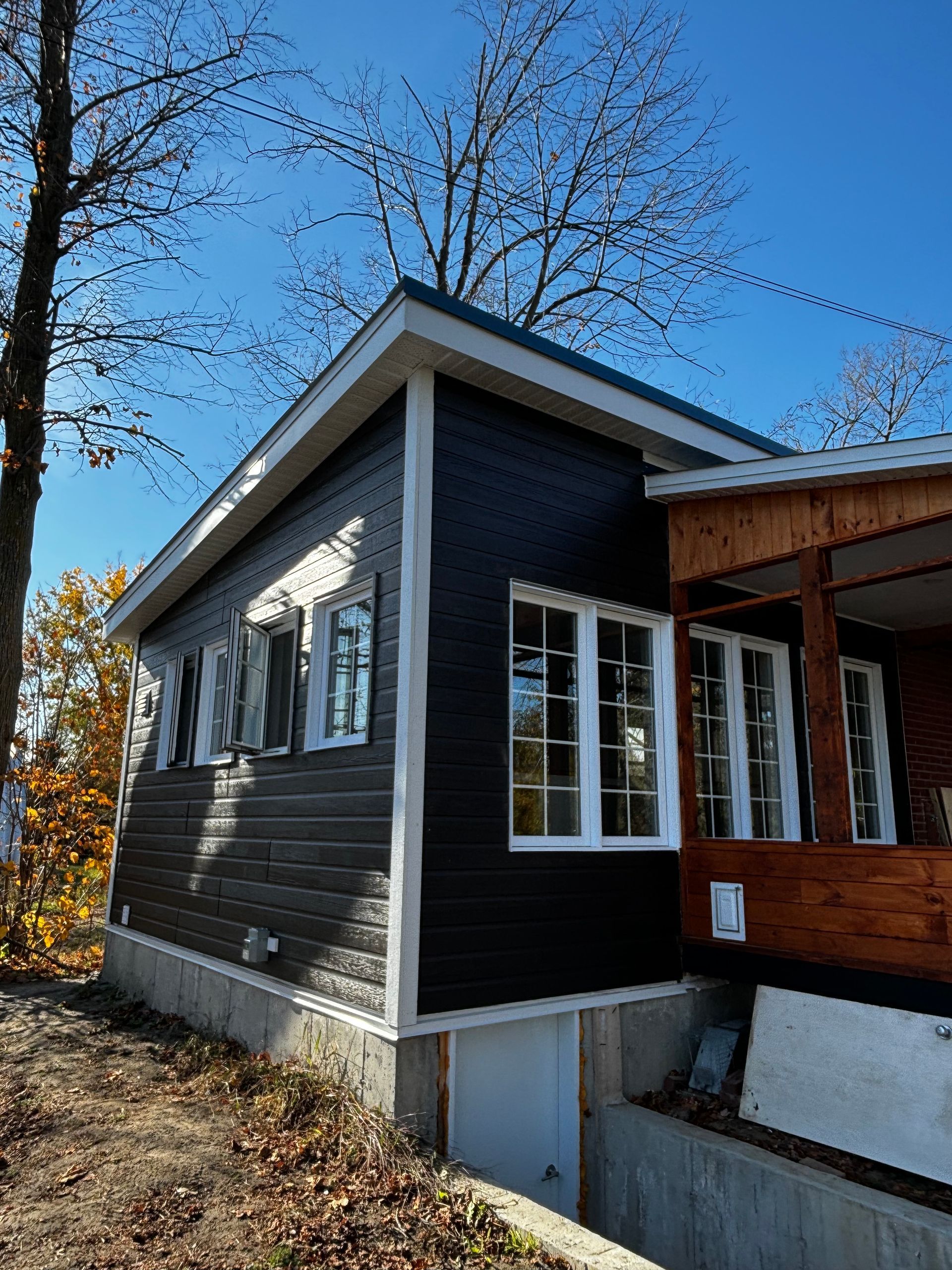 Maison gris foncé aux encadrements de fenêtres blancs et au porche en bois. Sur fond de ciel bleu éclatant.