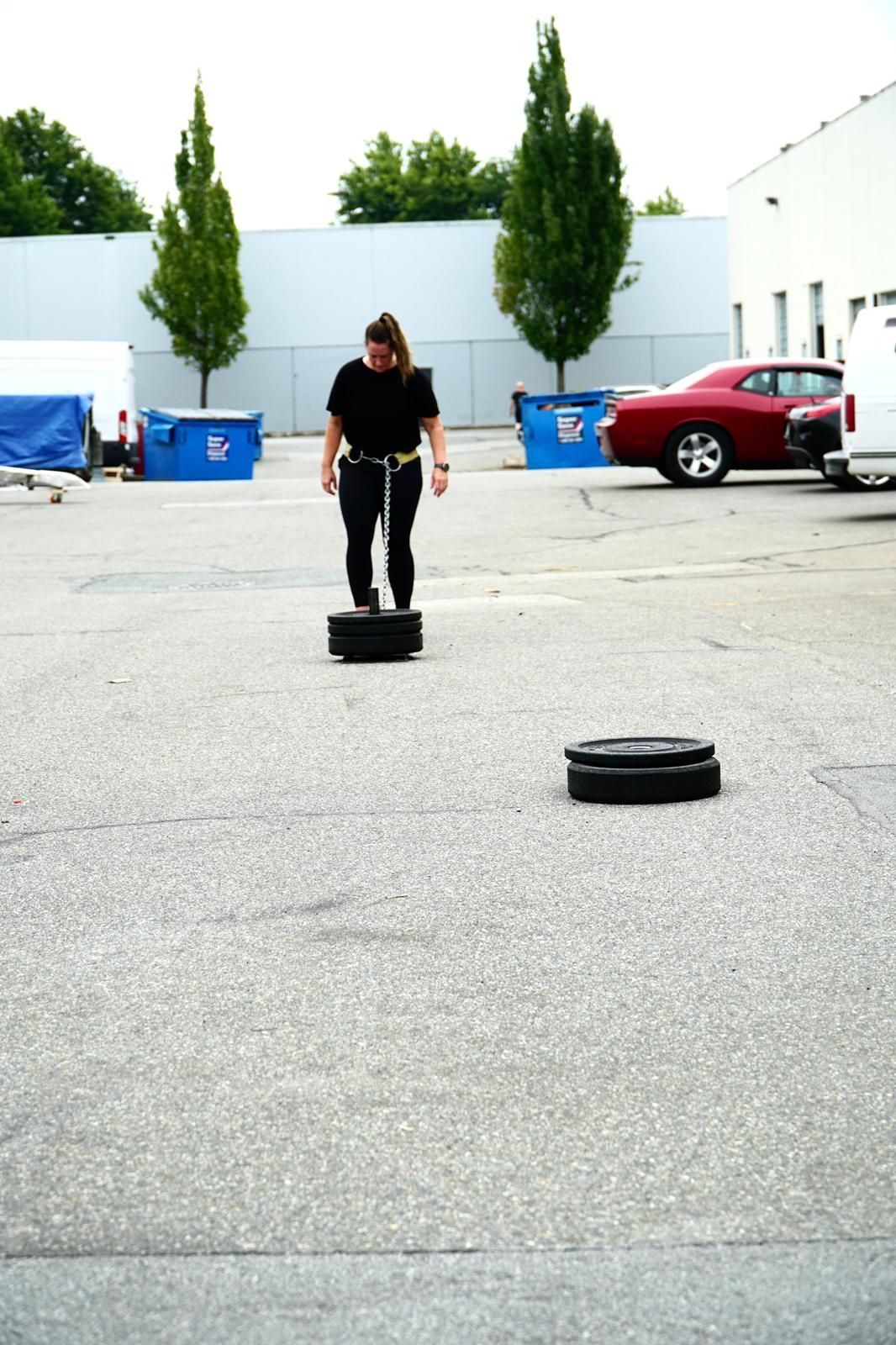 Woman balances on stacked tires in an outdoor parking lot; another stack of tires is in front of her.