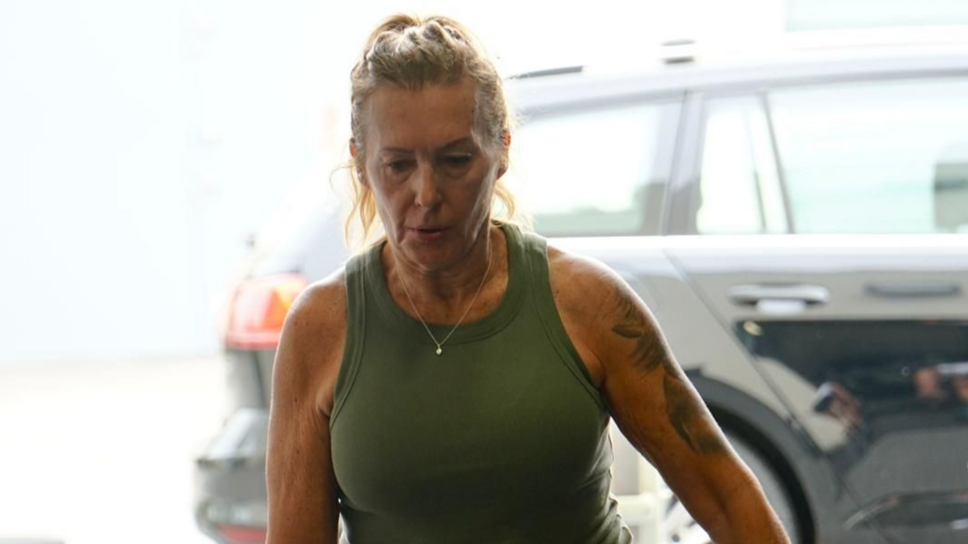 Woman with arm tattoo in green tank top, exiting a car.