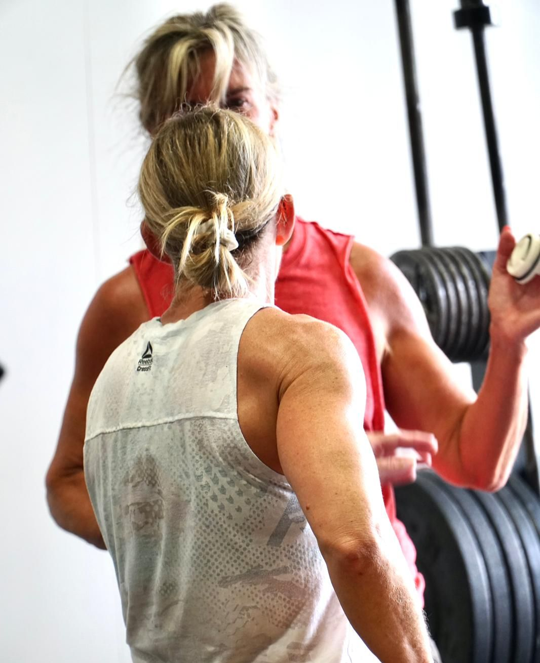 Two women in gym attire, one with a bun, are near weights.