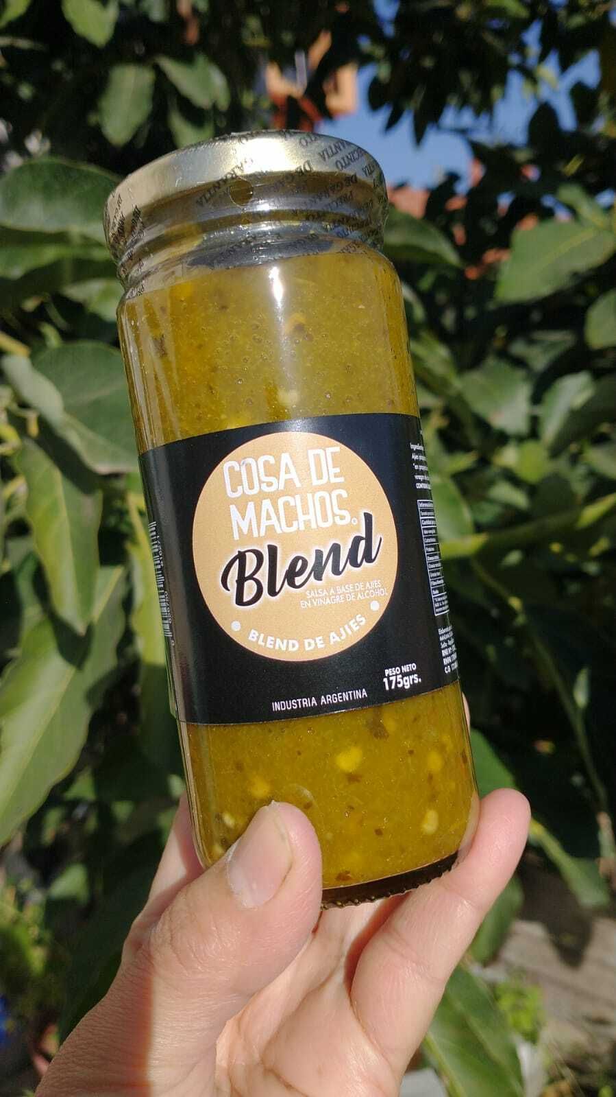 Una mano sosteniendo un frasco de salsa amarilla con la etiqueta "Mezcla de ajo y champiñones" al aire libre.