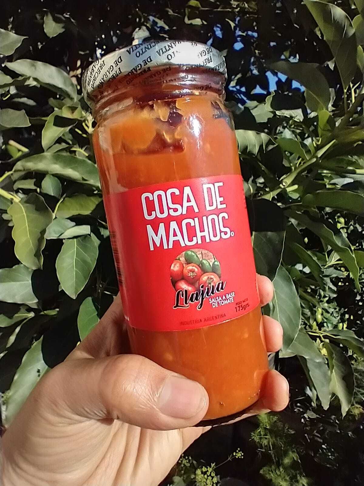 Una mano sostiene un pequeño frasco con la etiqueta “Cosa de Machos”, que contiene salsa de naranja