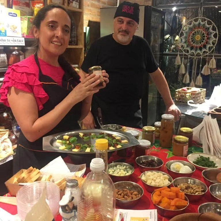 Dos personas detrás de una mesa de buffet con platos y bebidas variadas en un restaurante.