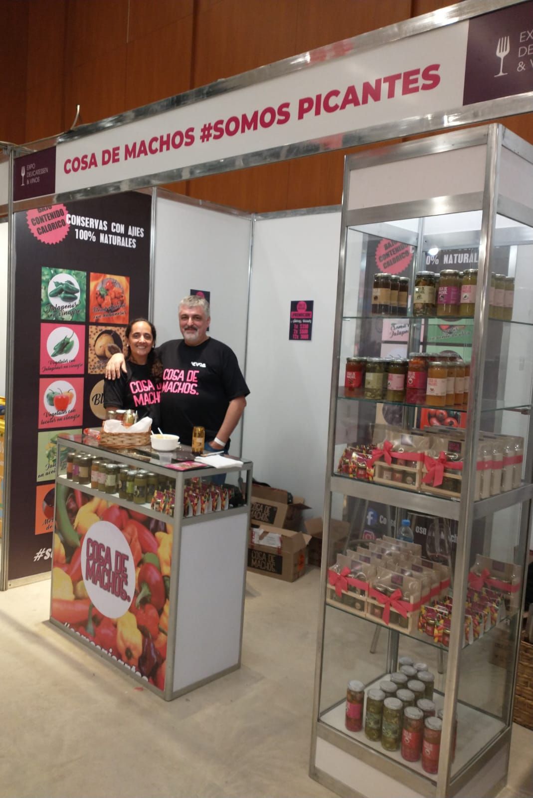Puesto de venta con dos vendedores que ofrecen aperitivos de encurtidos picantes y frascos en exhibición.