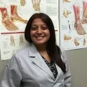 A woman in a lab coat is smiling in front of a wall with posters on it.