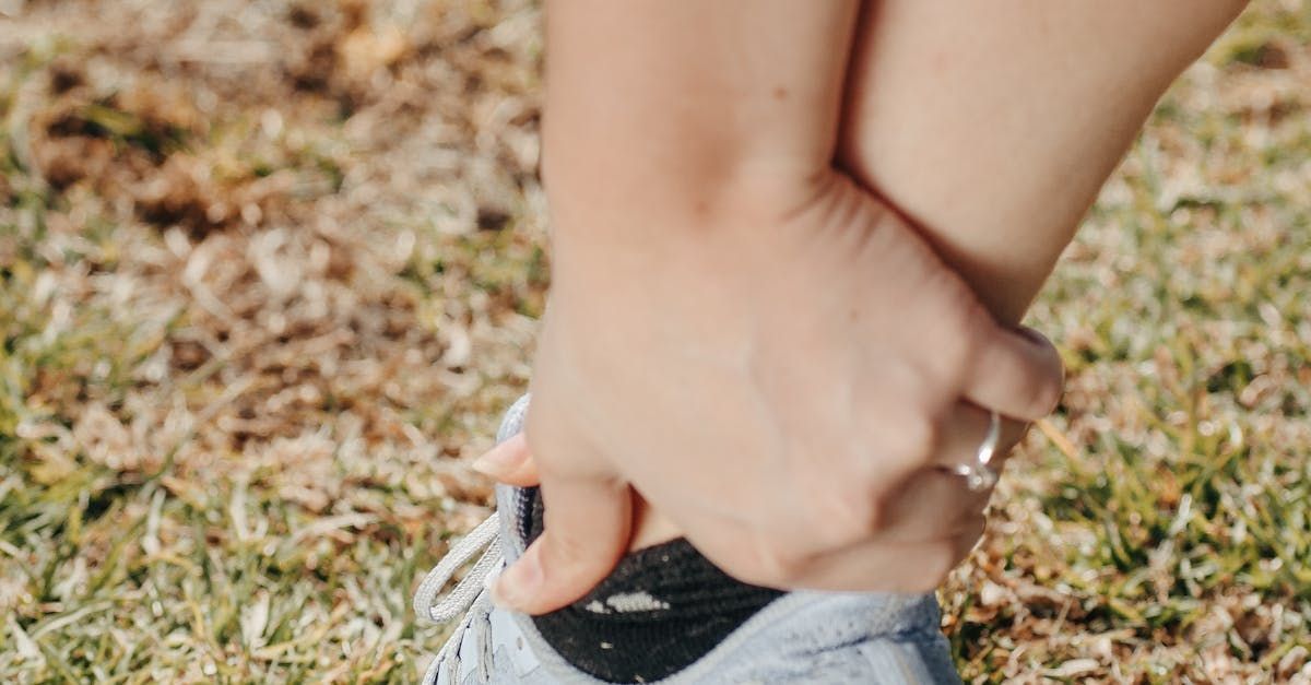 A woman is tying her shoelaces on a grassy field.