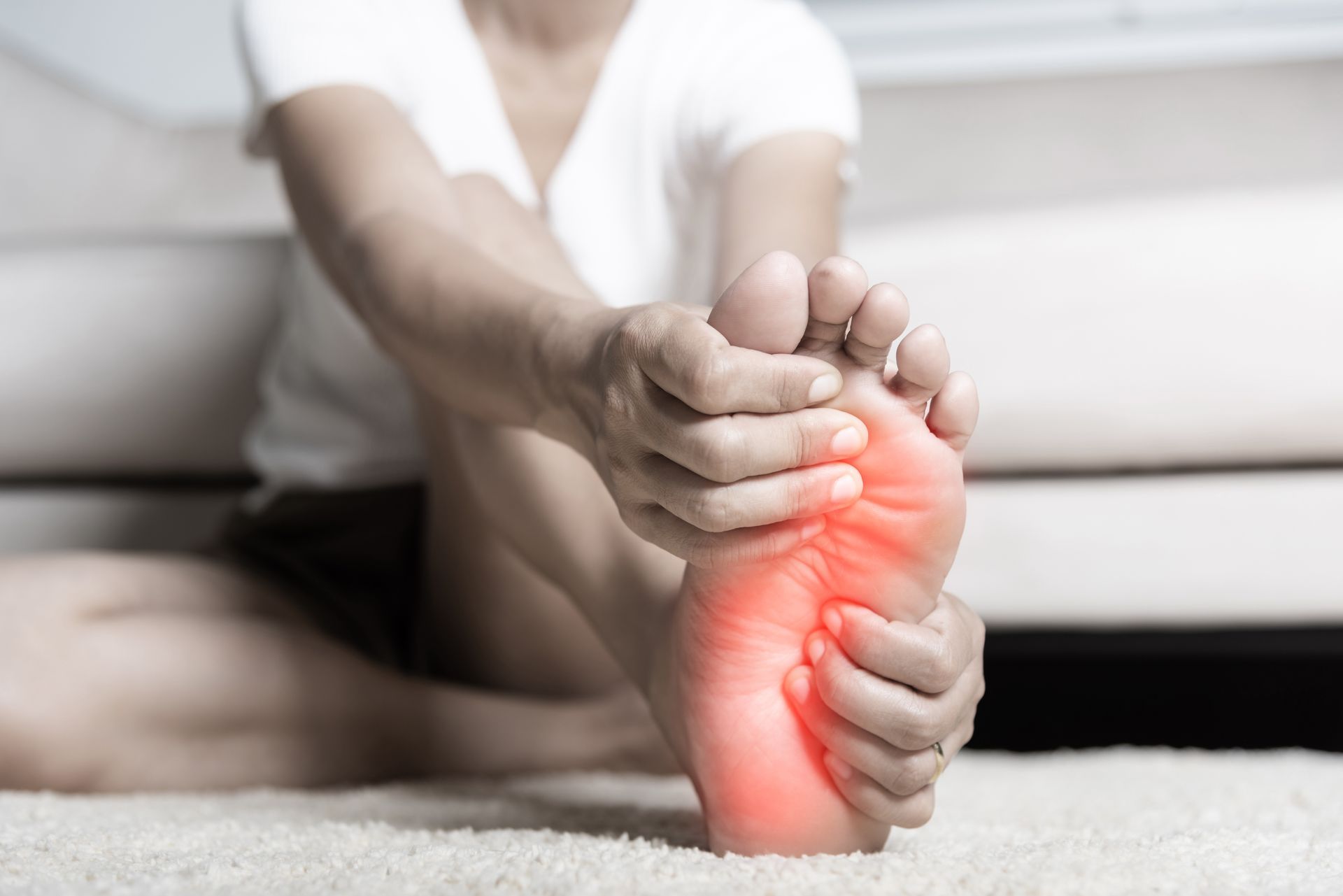 A woman is sitting on the floor holding her foot in pain.