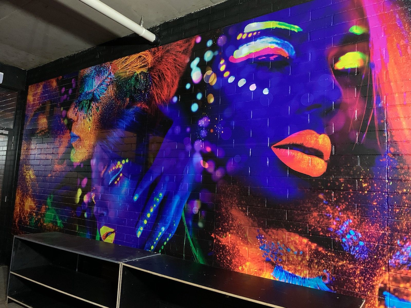 A glow in the dark painting of a woman 's face on a brick wall.