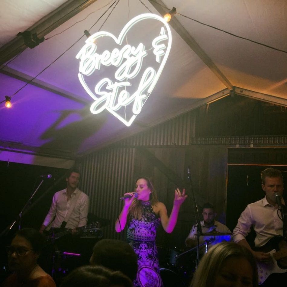 A woman singing into a microphone under a neon sign that says brezzy stef