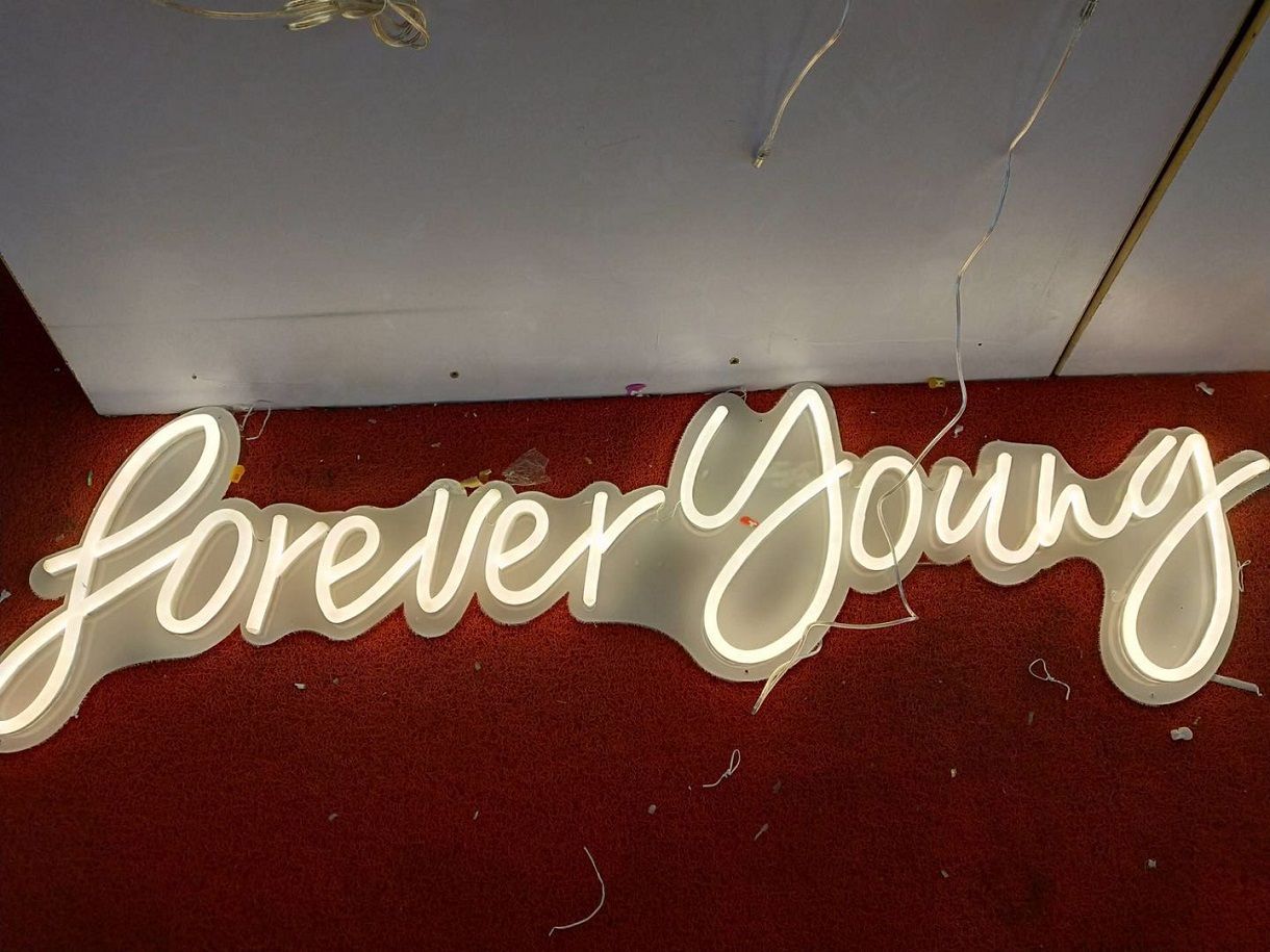 A neon sign that says forever young is hanging on a wall.