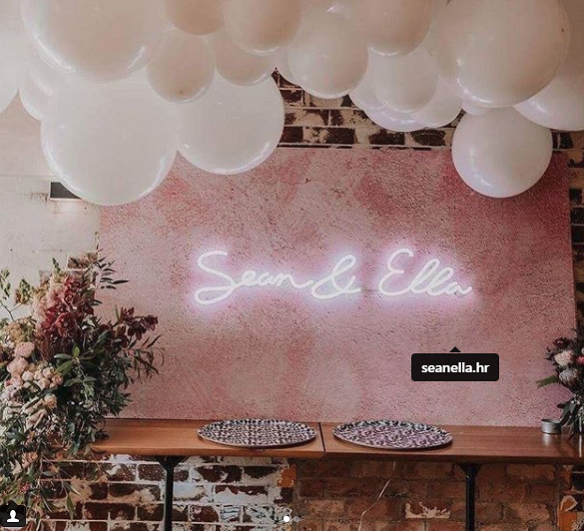 A pink wall with balloons and a neon sign that says sean & ella